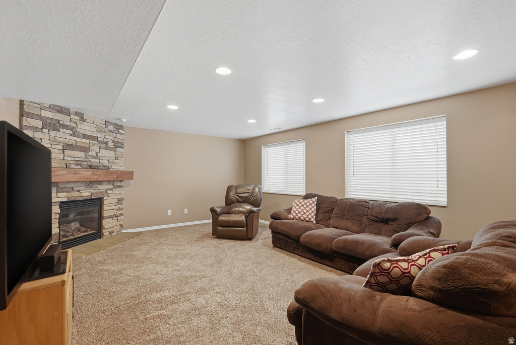 Living area featuring a stone-clad fireplace with a wood mantel, carpet flooring, recessed lighting, and multiple windows with blinds