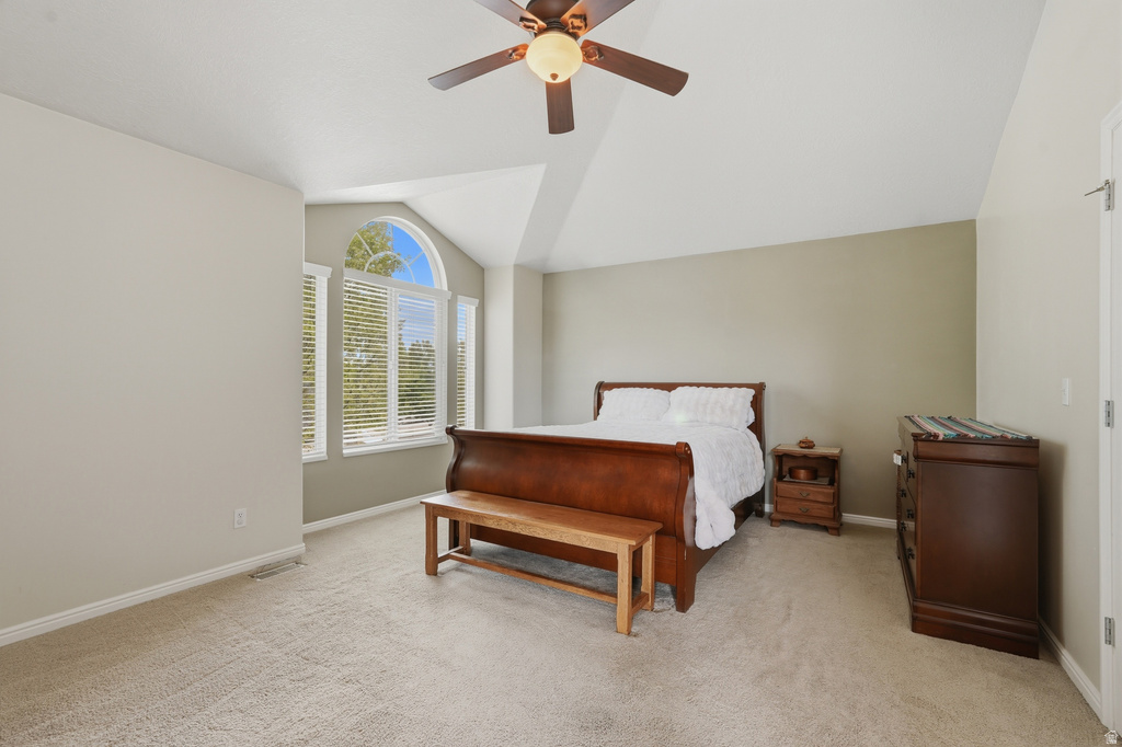 Vaulted ceiling room featuring an arched window, three pane windows with blinds, a ceiling fan, and light-toned carpet flooring