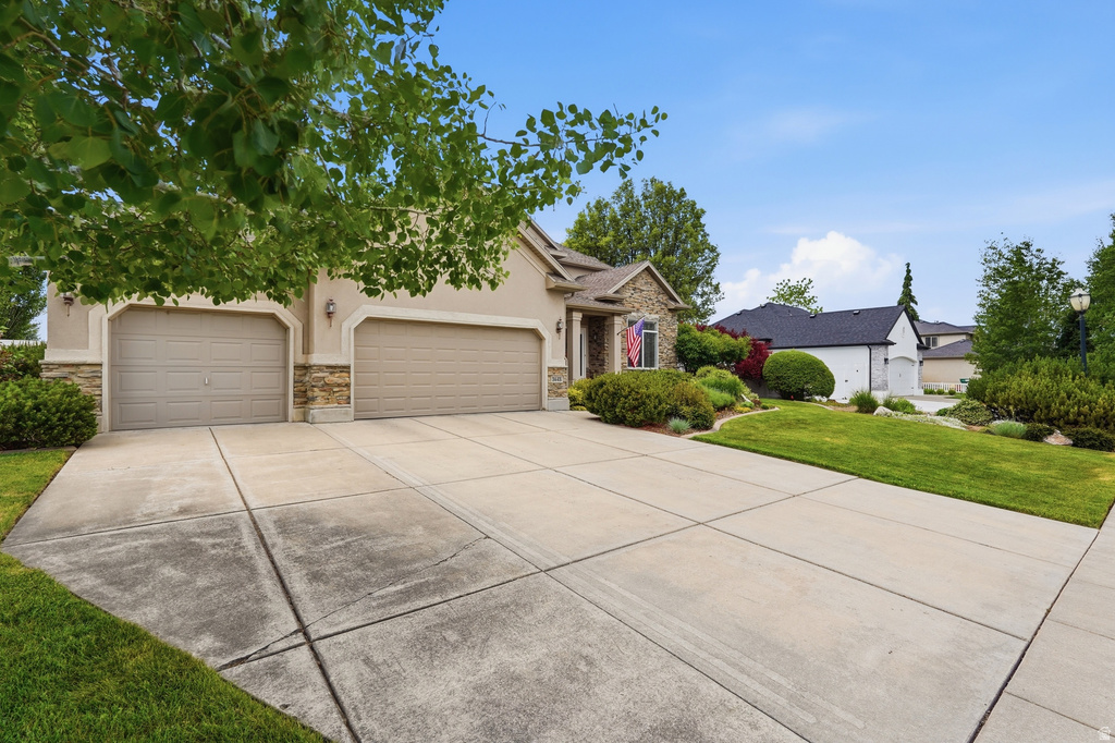 Front exterior featuring a stucco facade with stone accents, a two-car garage, and an expansive concrete driveway
