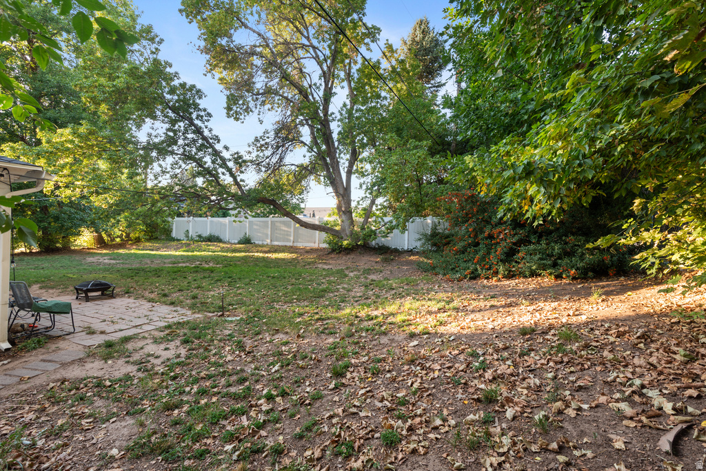 Expansive backyard featuring a partial stone patio, mature trees, and a white privacy fence