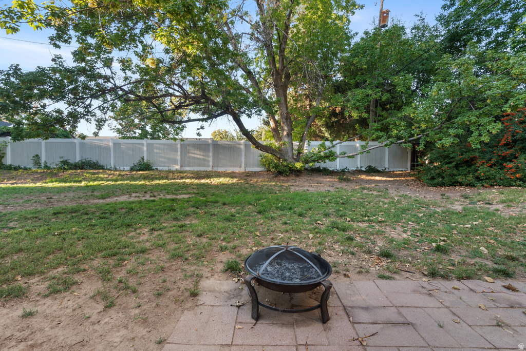 Expansive backyard featuring a fire pit on a paver patio, a partial lawn area, mature trees, and a white privacy fence