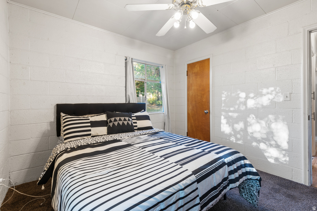Bedroom featuring textured white block walls, dark carpeting, and a single window offering natural illumination
