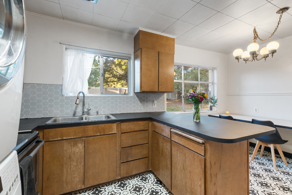 Kitchen area featuring wood cabinetry, dark countertops, a double basin stainless steel sink, and a gray hexagonal tile backsplash