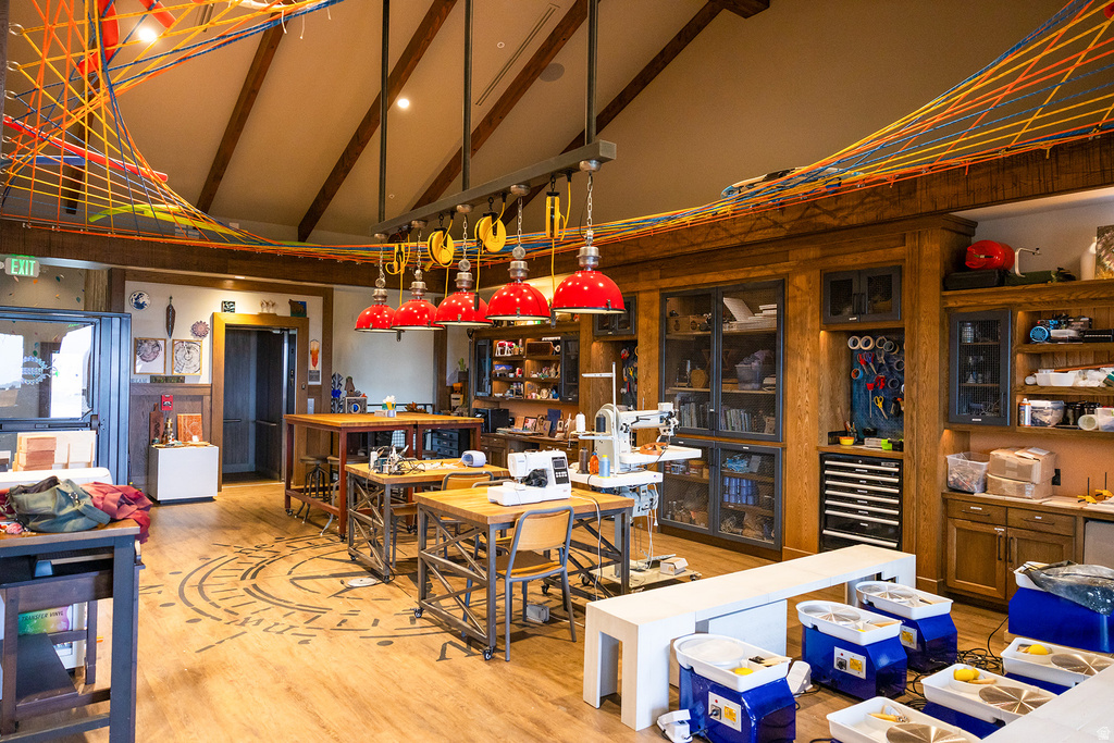 Spacious room featuring vaulted ceilings with exposed beams, wood-finish flooring, and extensive built-in wooden cabinetry with glass-front display sections