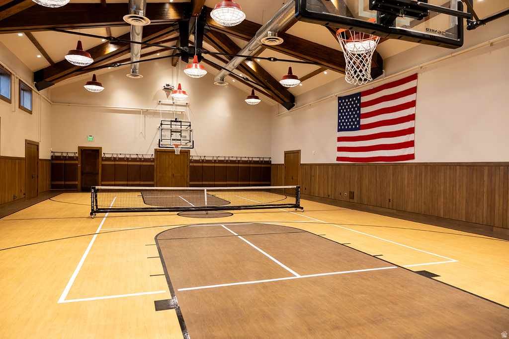 Indoor sports court featuring a basketball hoop, a net, wood-finish flooring, exposed beam ceilings, and industrial pendant lighting