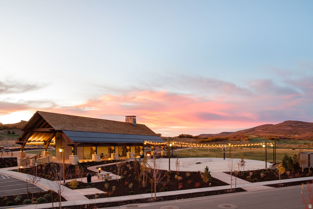 Stone and timber-clad clubhouse featuring an expansive covered patio, an outdoor gathering space with string lighting, and landscaping with low-lying shrubs