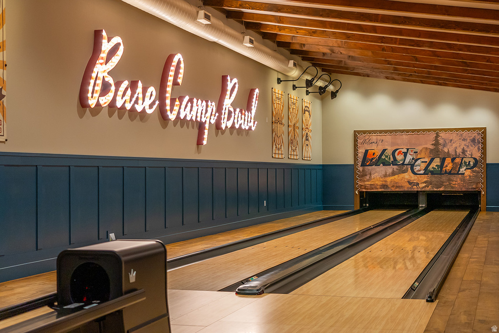 Private two-lane bowling alley featuring wood-finish flooring, exposed wood ceiling beams, and decorative wall paneling