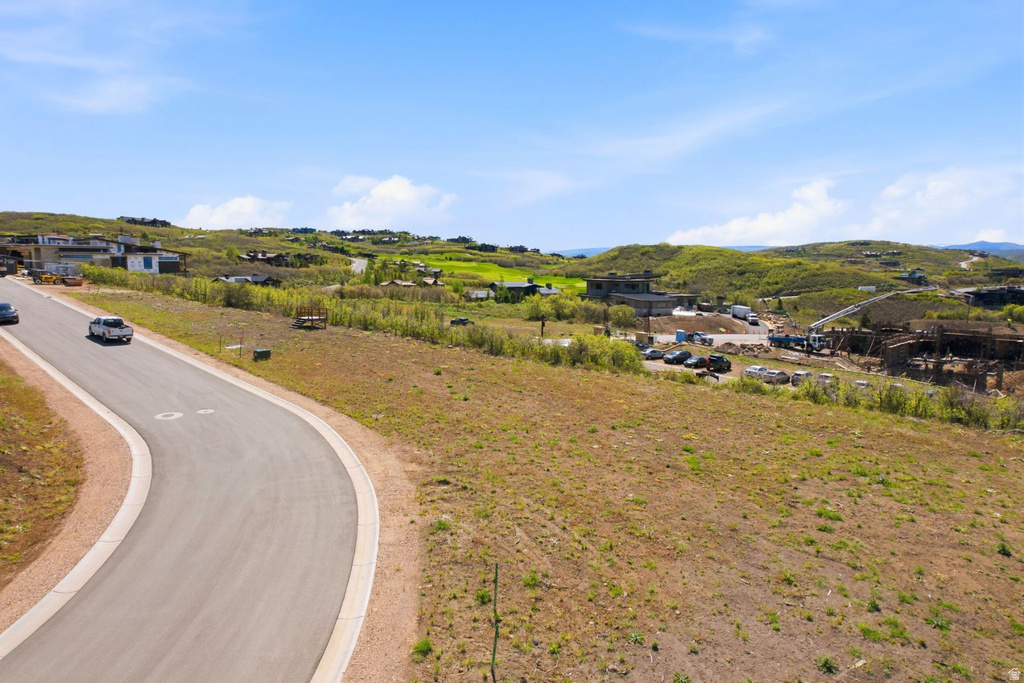 Expansive hillside lot featuring varying topography, paved roadway, scattered residential structures, and natural green landscaping