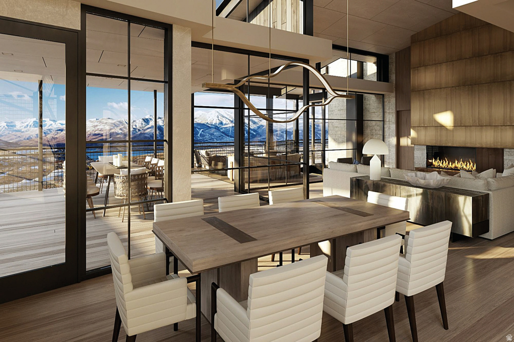 Open-concept dining and living area featuring expansive floor-to-ceiling windows, wood-finish flooring, a contemporary linear fireplace with a stone surround, and an integrated wood paneled accent wall