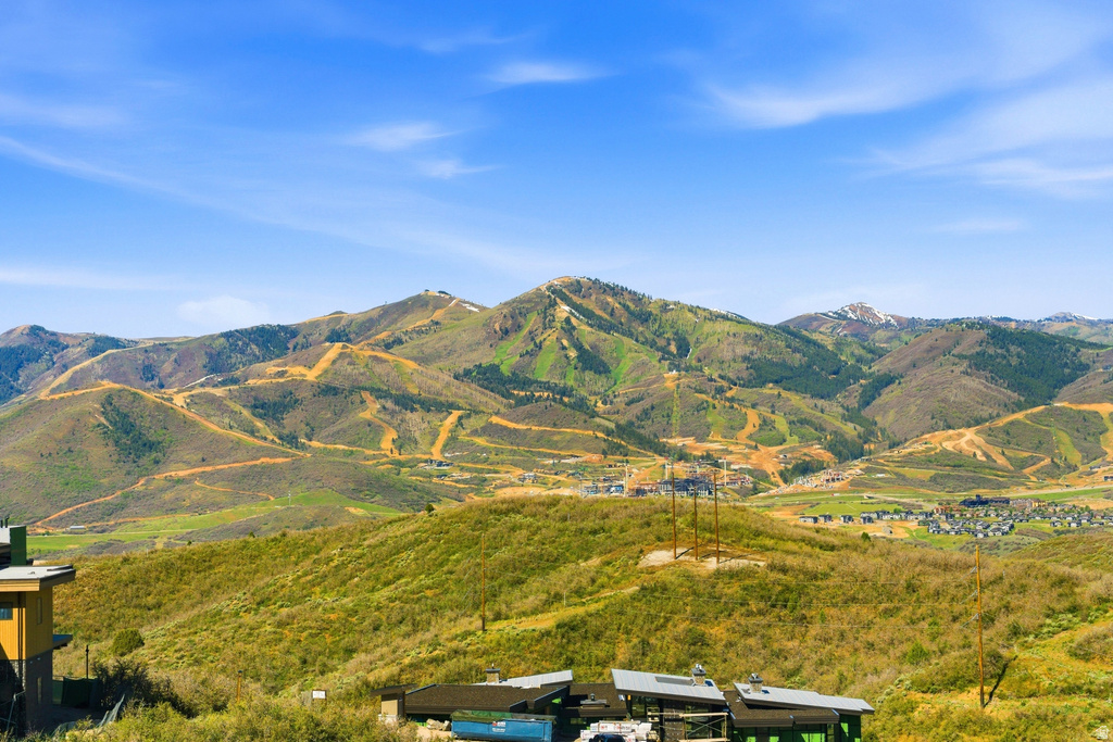 Expansive mountain landscape featuring varied green and brown foliage, distant structures, and a clear blue sky