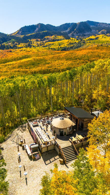 Expansive outdoor deck with a central yurt structure, surrounded by an extensive forest with mountainous topography in the background