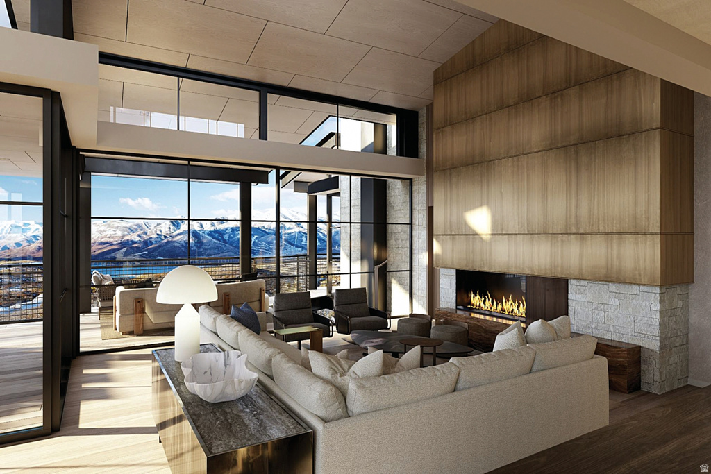 Great room featuring a vaulted ceiling with exposed beams, wood-finish flooring, a contemporary fireplace with a stone surround, and expansive windows offering mountain scenery