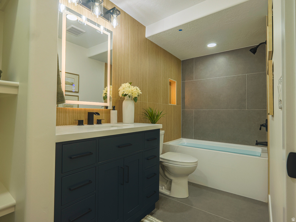 Modern bathroom featuring a dark blue vanity with a white countertop, an illuminated rectangular mirror, and a bathtub with large format gray wall tiling