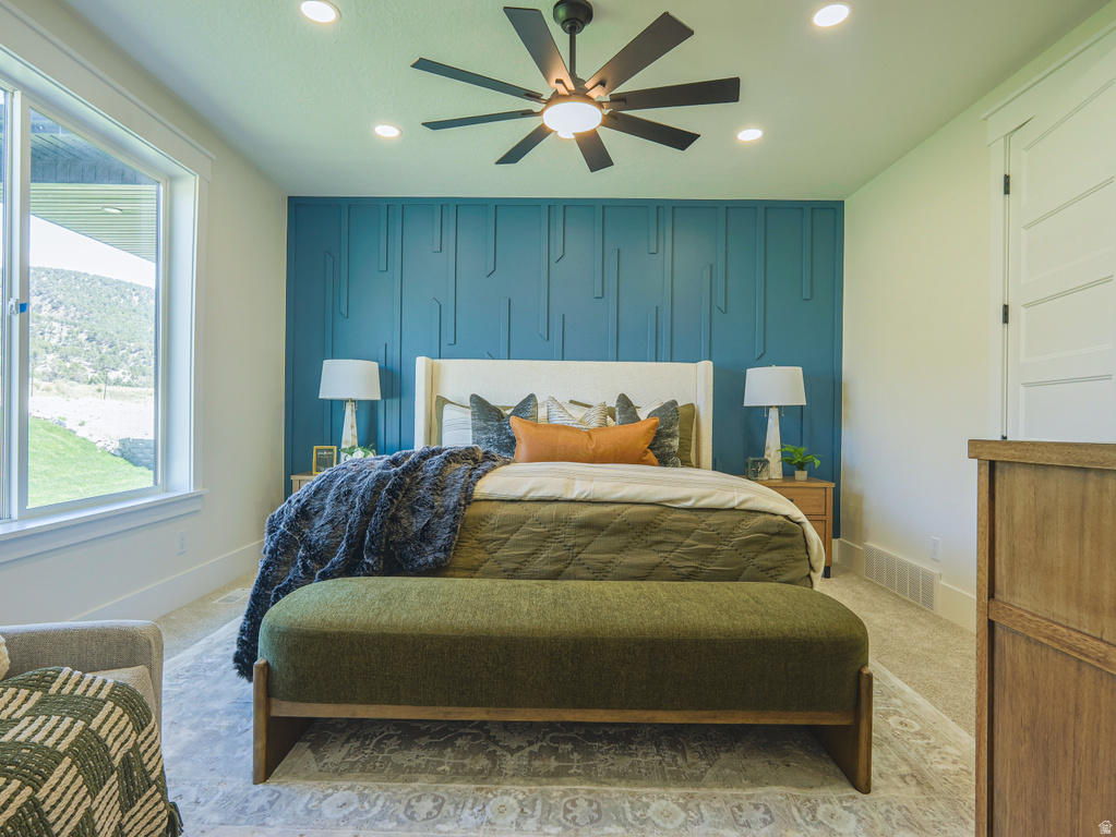 Accent wall featuring geometric paneling, large window with outdoor landscape, recessed ceiling lighting, ceiling fan with light, and light-tone carpeting