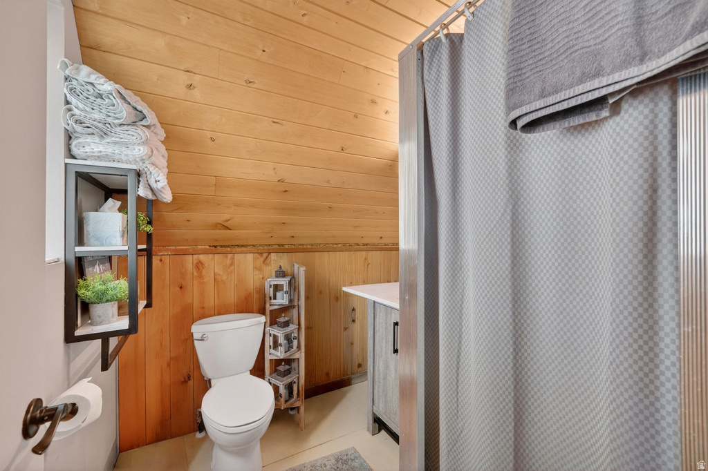 Bathroom featuring wood paneling, white toilet, vanity with integrated sink, shower with curtain, and wall-mounted shelving
