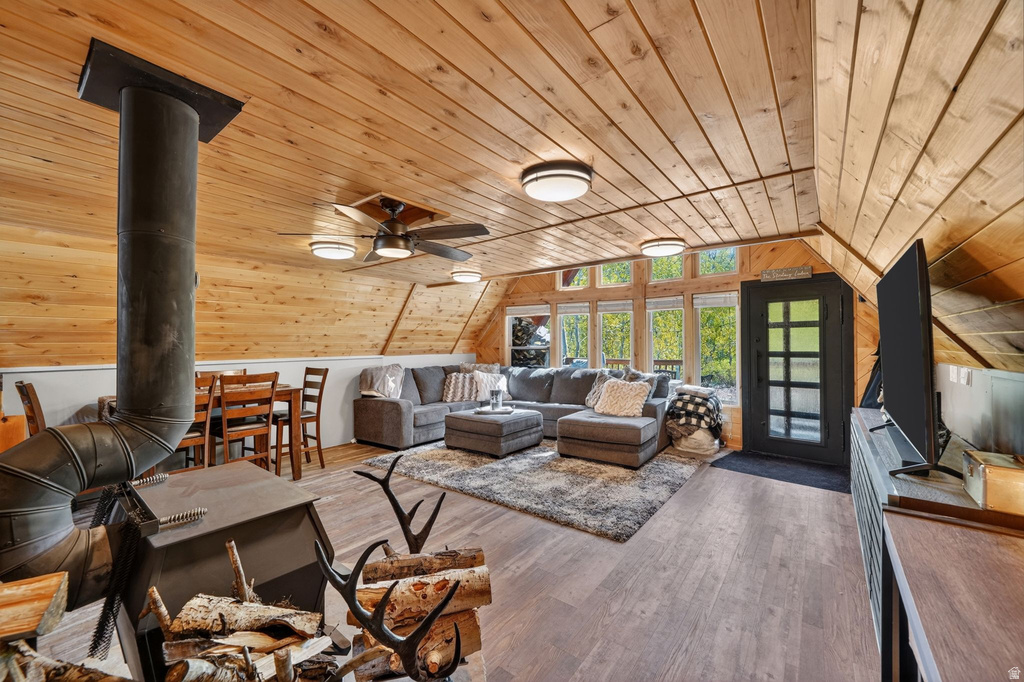 Spacious living area featuring a wood stove, vaulted wood-paneled ceilings, and wood-finish flooring