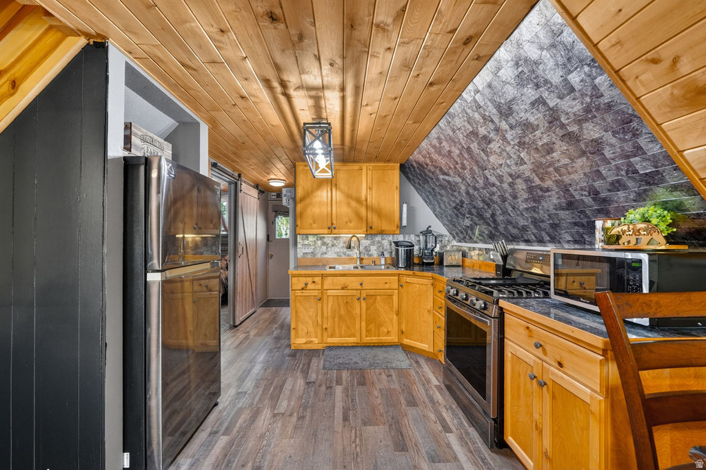 Kitchen featuring wood-finish flooring, natural wood cabinetry, dark countertops, and stainless steel appliances