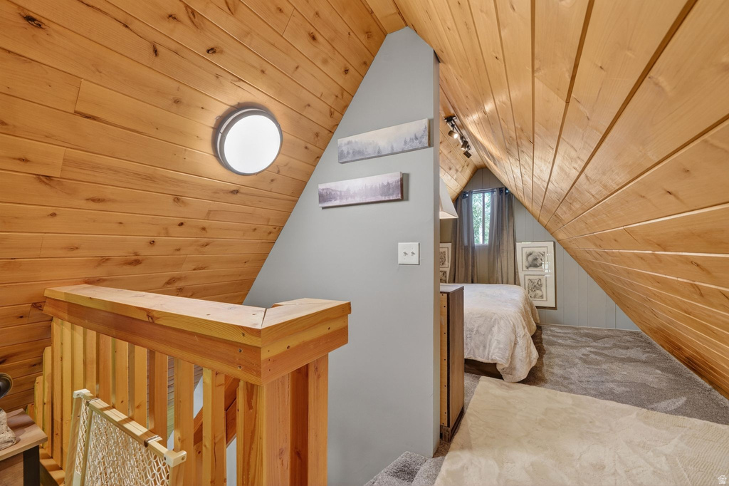 Attic space featuring natural wood-paneled walls and ceiling, a built-in wood railing, and a window with natural light