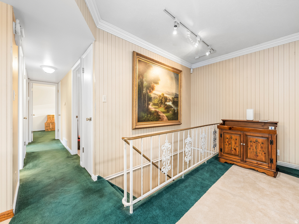 Hallway featuring vertical striped wallpaper, crown molding, track lighting, and a decorative railing