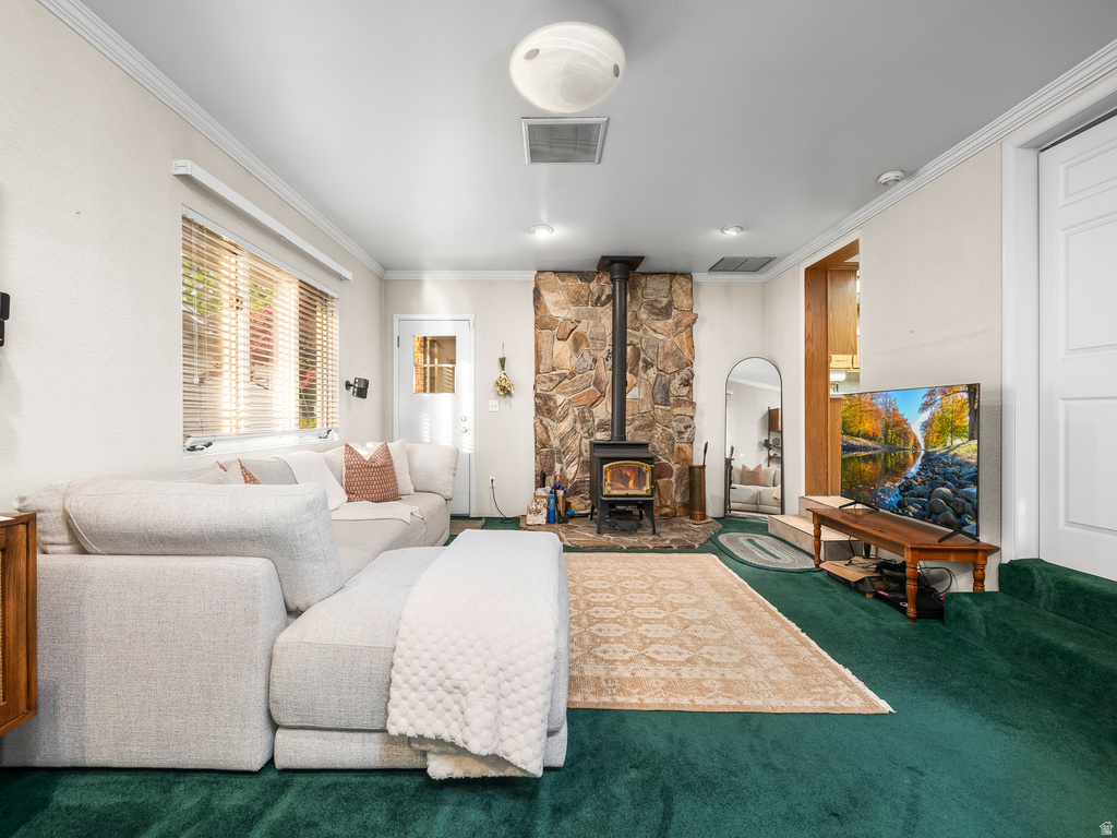 Living area featuring a stone accent wall with a wood-burning stove, crown molding, a recessed light, and a window with blinds