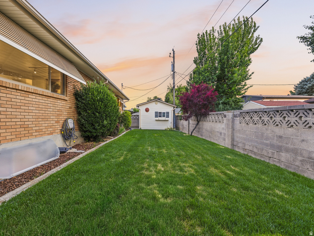 Expansive grassy yard area featuring a concrete block privacy fence with decorative caps, a white utility shed, and mature perimeter landscaping