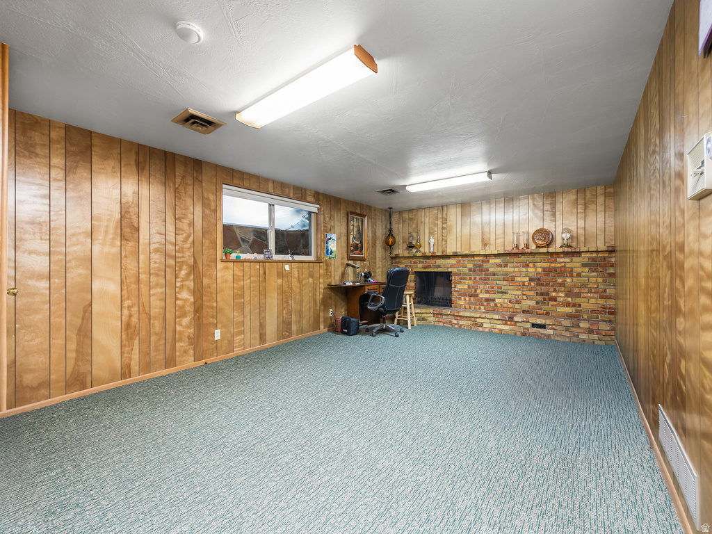 Spacious room featuring paneled walls, a brick fireplace, a window, and light blue patterned carpeting