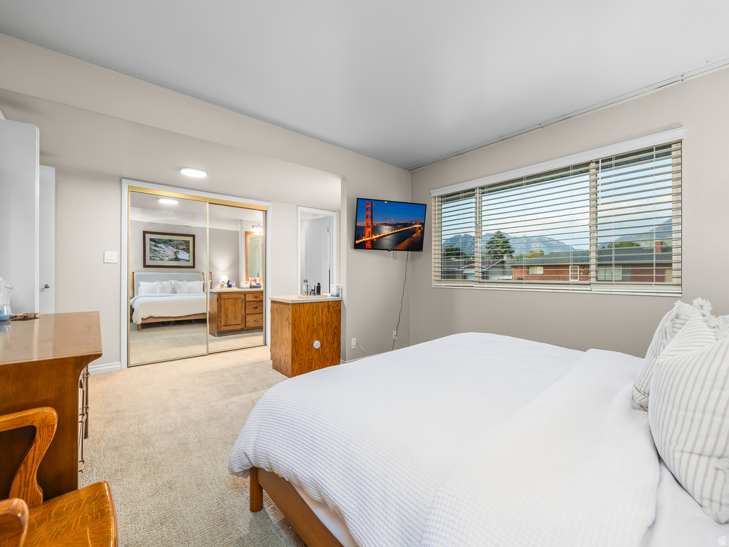 Bedroom with neutral carpeting, large window with horizontal blinds, and a mounted flat-screen television