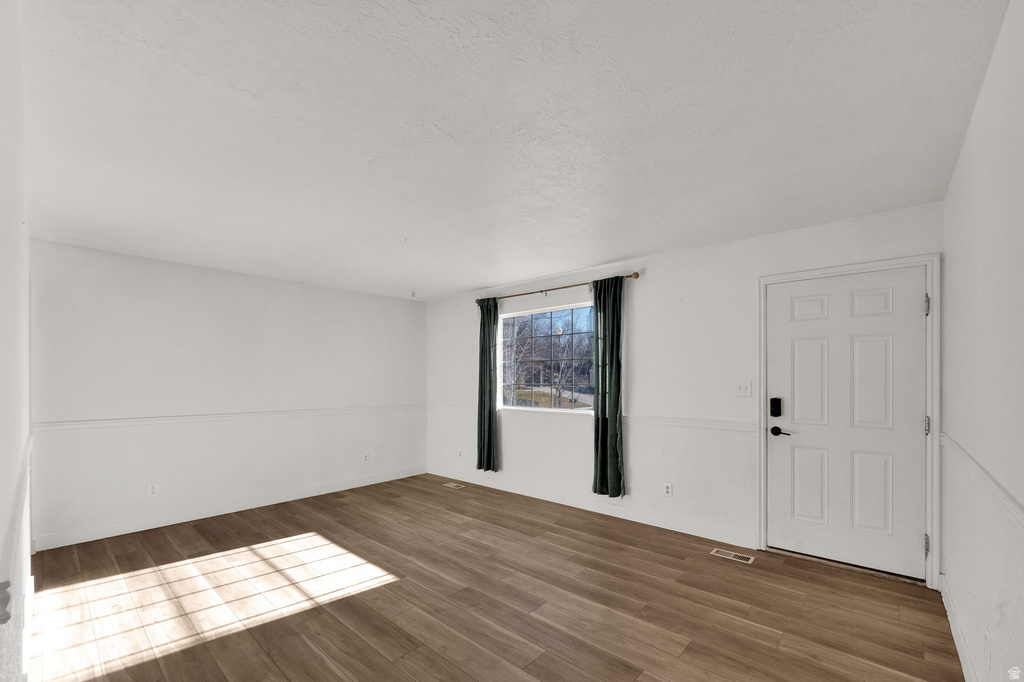 Wood-finish flooring, white paneled door with black hardware, and a window with dark curtains