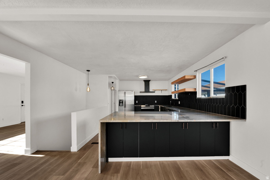 Kitchen featuring a large island with stone countertops, dark cabinetry, wood-finish flooring, a geometric tile backsplash, and open shelving