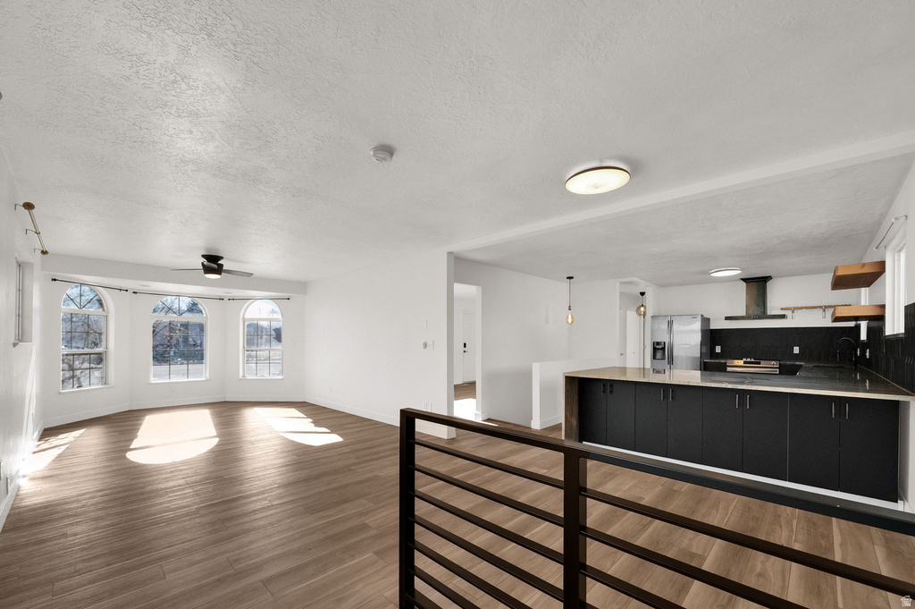 Spacious interior featuring wood-finish flooring, a contemporary kitchen with dark cabinetry, stainless steel appliances, and a kitchen island with a light-toned countertop
