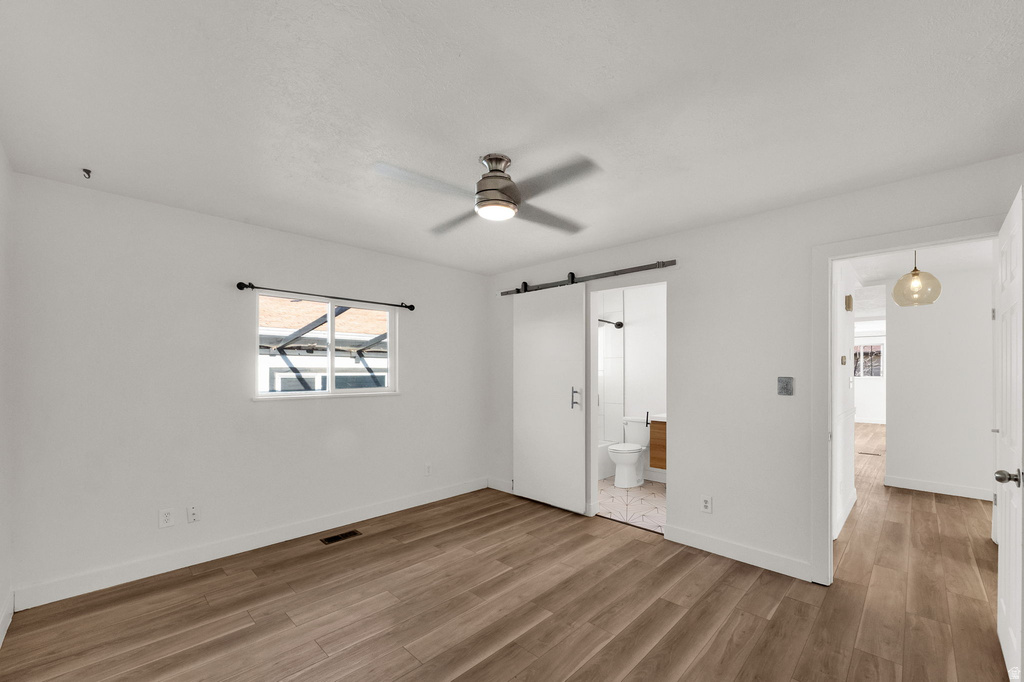 Wood-finish flooring, ceiling fan with integrated lighting, a sliding barn door, and a single window with a dark curtain rod