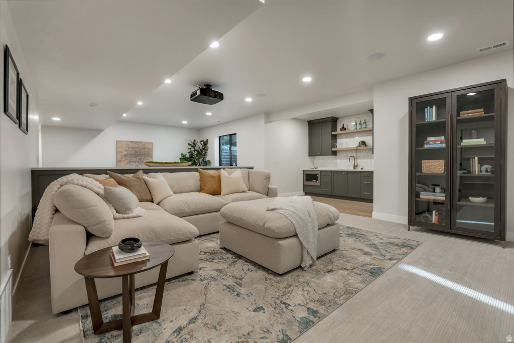 Spacious entertainment area featuring recessed lighting, a ceiling-mounted projector, and a built-in wet bar with dark cabinetry, open shelving, and a stainless steel sink