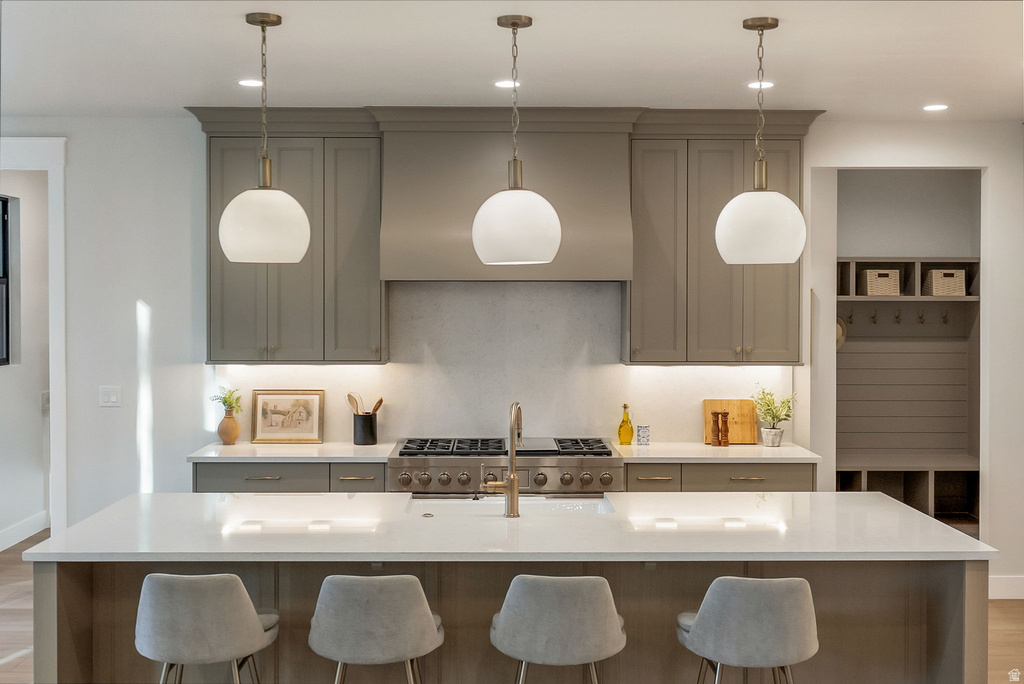 Kitchen featuring a central island with countertop seating, three pendant lights, stainless steel range with matching hood, gray cabinetry, and light-toned countertops