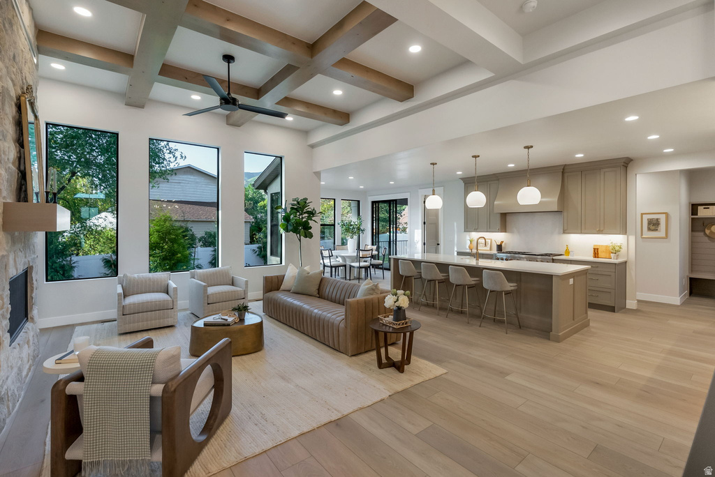 Expansive living area featuring a coffered ceiling with wood beams, a stone-faced fireplace, a modern kitchen island with seating, a built-in kitchen hood, and large vertical windows