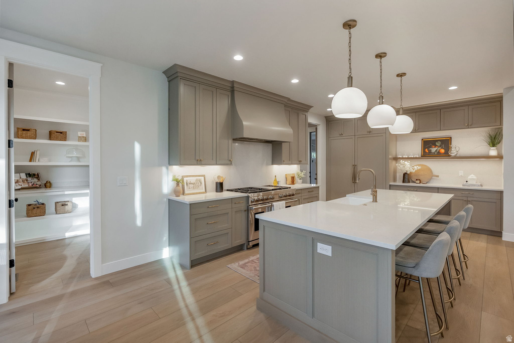Gourmet kitchen featuring a substantial island with seating, pendant lighting, professional-grade range with hood, custom cabinetry, and wood-finish flooring