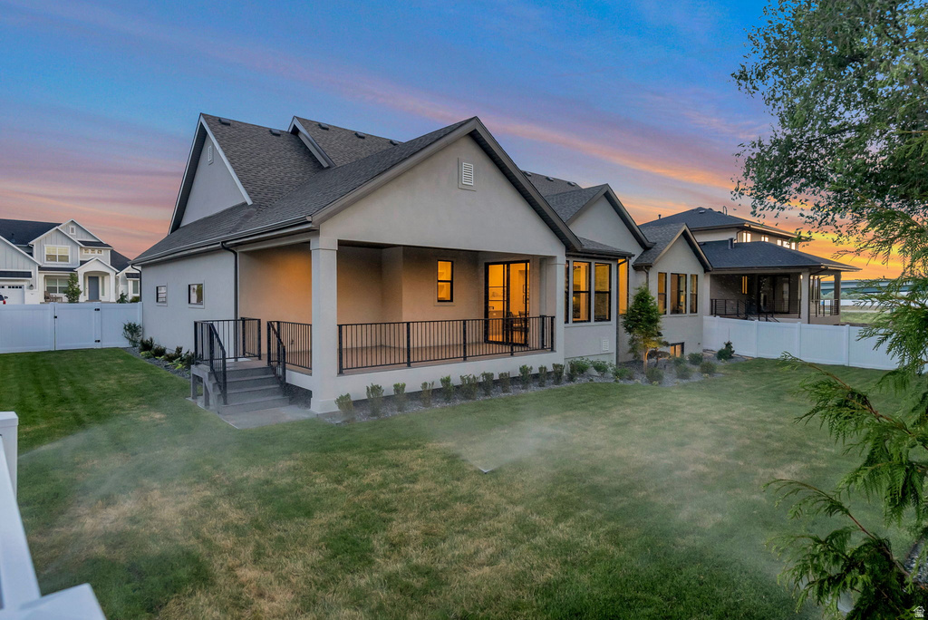 Rear elevation featuring a covered patio with black railings, a spacious lawn, and a white privacy fence