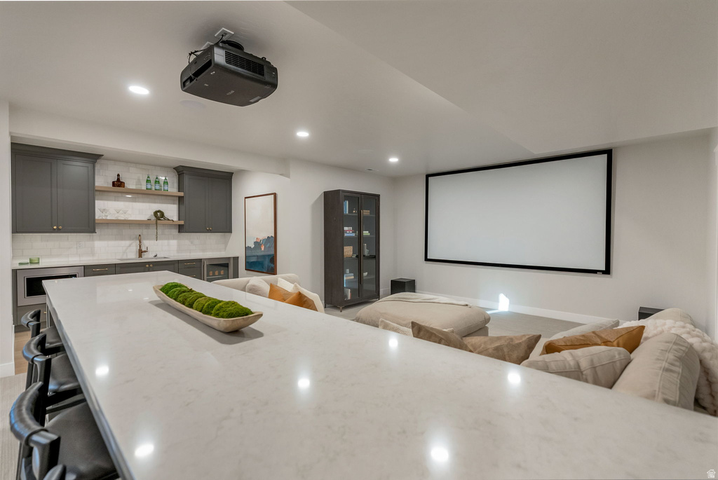 Spacious entertainment area featuring a large projection screen, ceiling-mounted projector, and a wet bar with gray cabinetry, white subway tile backsplash, and open shelving