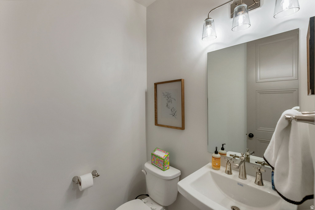 Powder room featuring a pedestal sink, brushed nickel faucet, wall-mounted mirror, and three-light vanity fixture
