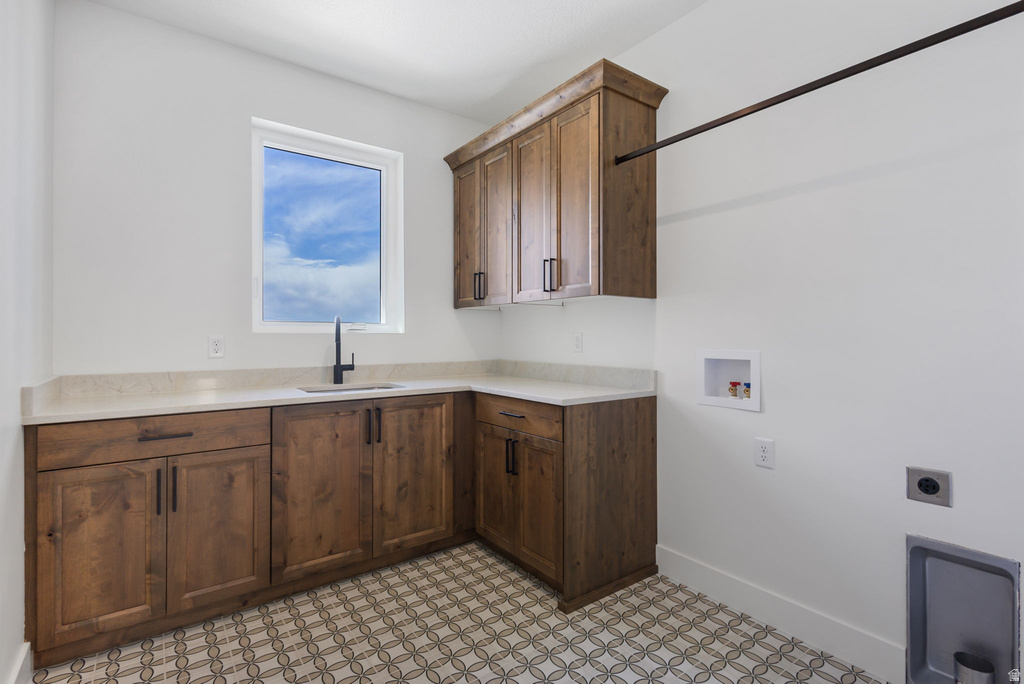 Laundry area featuring wood cabinetry, light-toned countertops, a matte black faucet, and patterned floor tiles