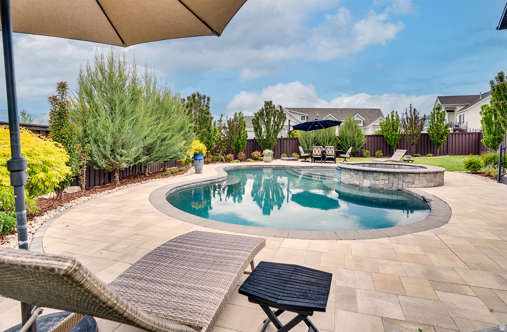 Curved swimming pool with an integrated stone-clad spa, surrounded by extensive paver patio