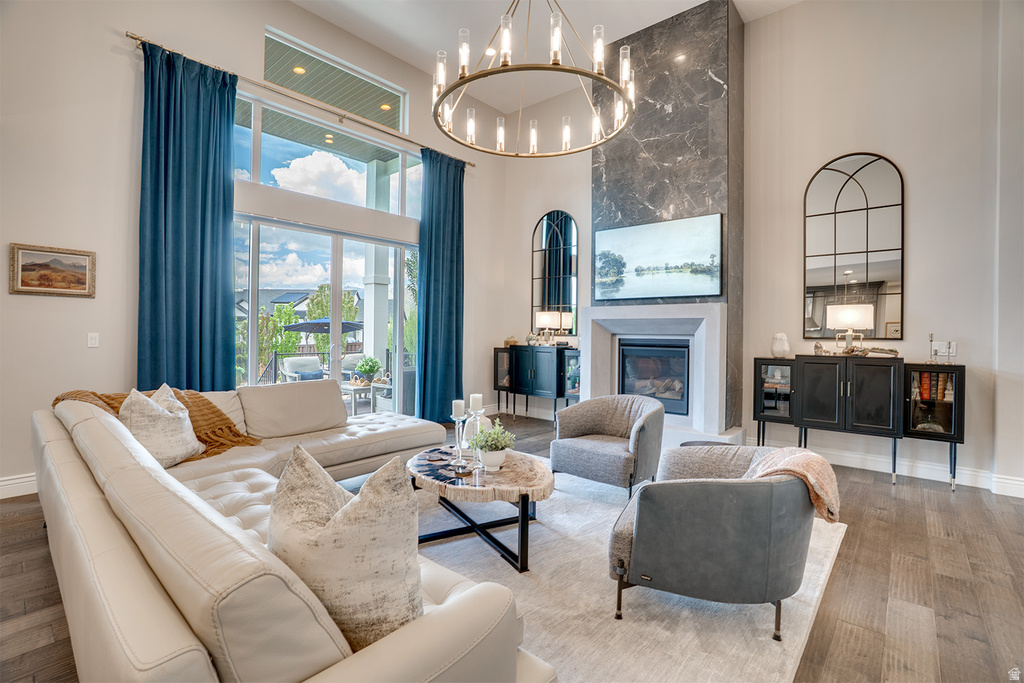 Spacious living area featuring a two-story ceiling, a contemporary chandelier, a fireplace with a stone-clad chimney extending to the ceiling, wood-finish flooring, and large sliding glass doors providing access to an outdoor area