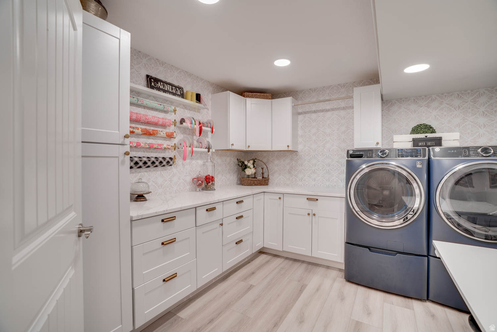 Laundry room featuring light wood-finish flooring, white cabinetry with bronze hardware, white countertops, and a patterned wall covering