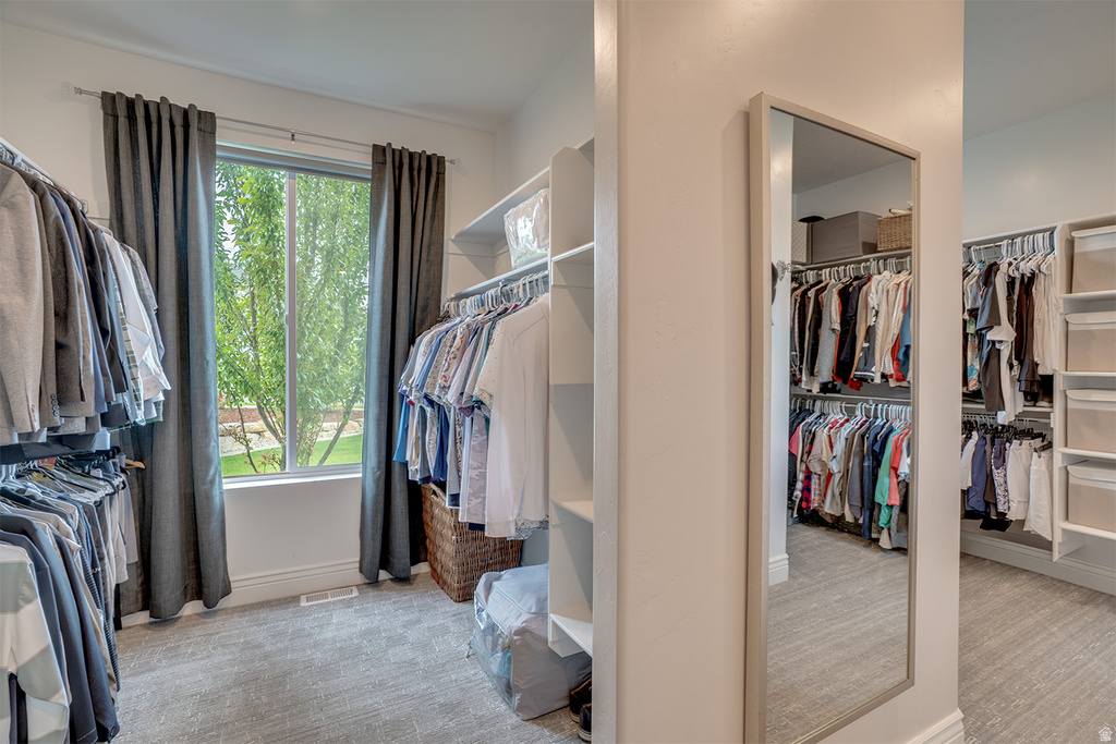 Spacious closet featuring carpet flooring, built-in shelving, hanging rods, and a large window with privacy curtains