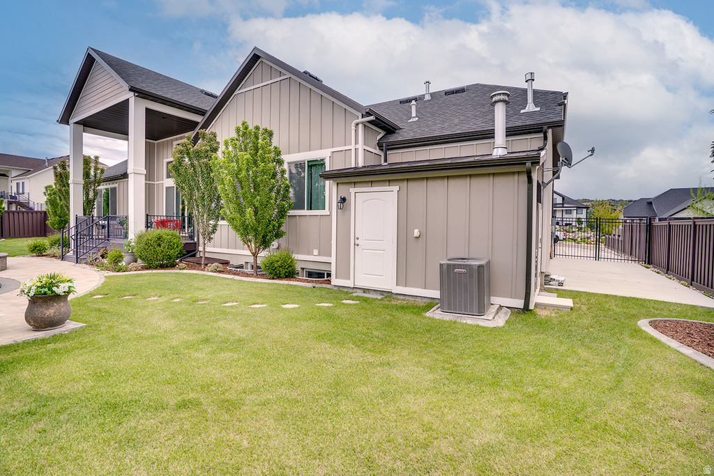 Spacious backyard featuring a manicured lawn, paved patio, mature trees, and a covered porch with dark railings