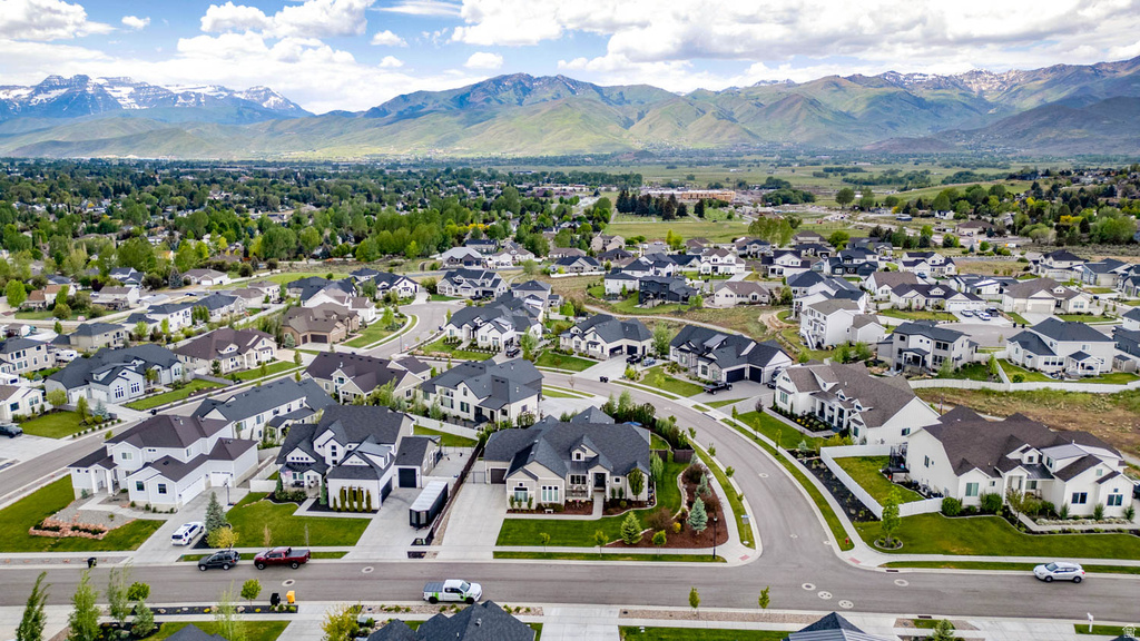 Expansive residential development featuring contemporary homes, curved streets, verdant landscaping, and distant snow-capped mountains