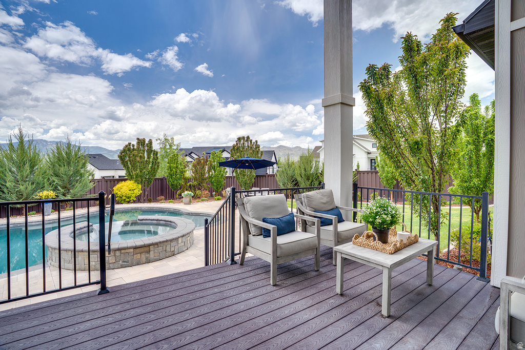 Expansive outdoor living area featuring a composite deck, covered patio, fenced swimming pool, integrated hot tub with stone surround, and mature perimeter landscaping