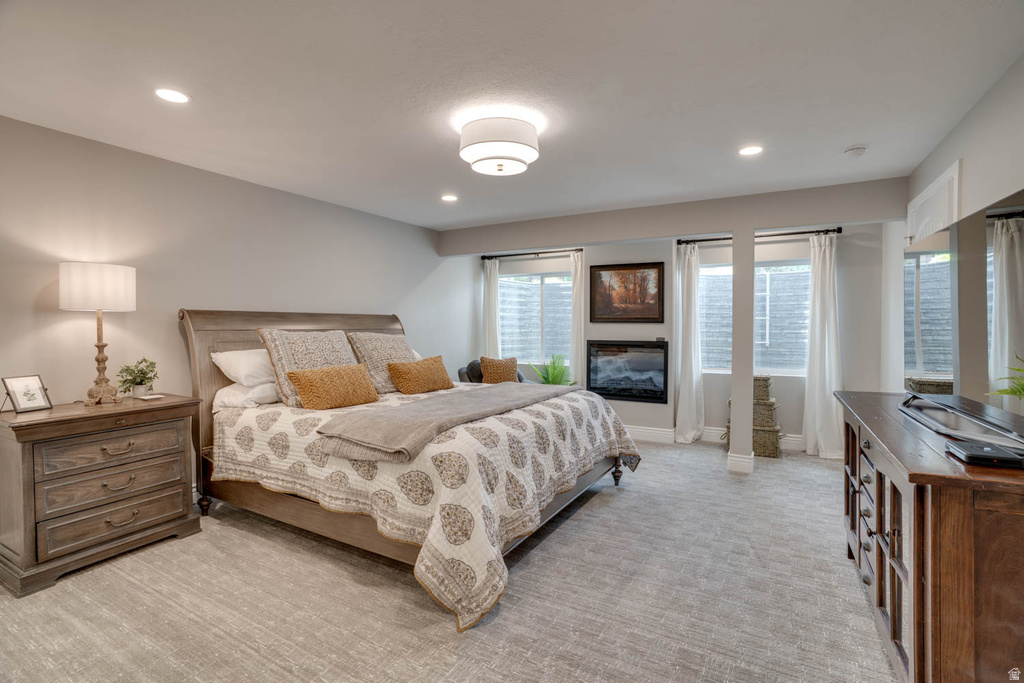 Bedroom featuring light gray walls, recessed lighting, a ceiling-mounted light fixture, three windows with white curtains, a built-in fireplace, and light-toned carpet flooring