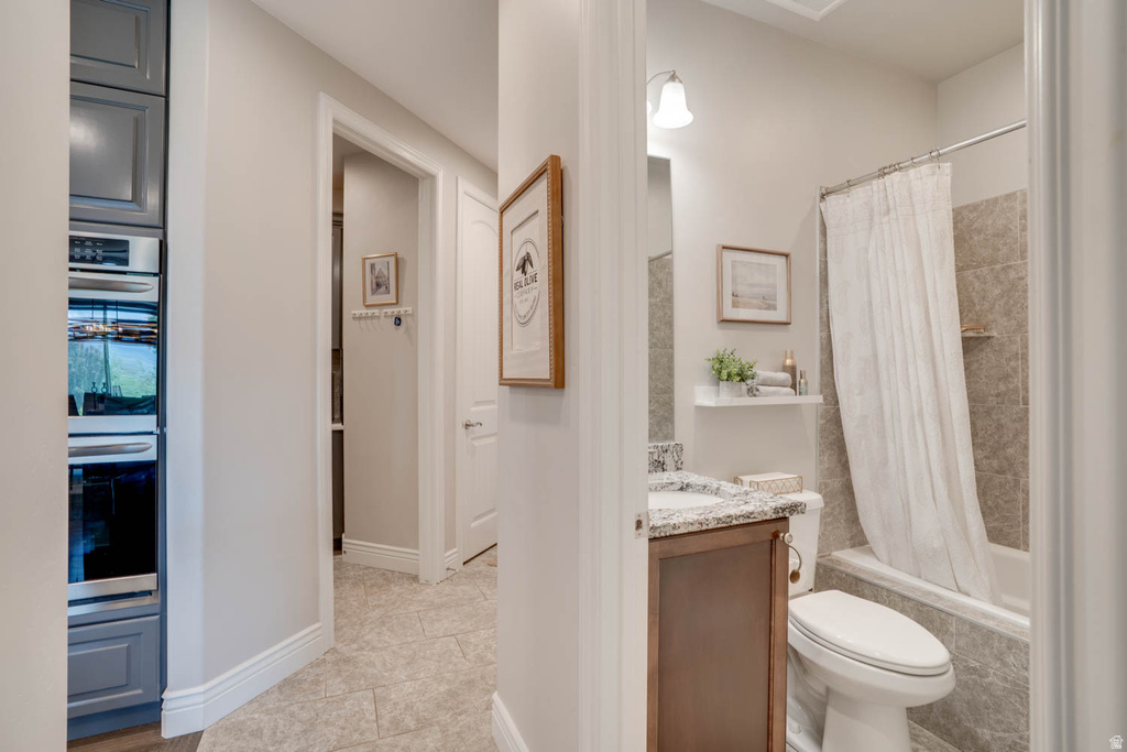 Hallway featuring built-in double ovens, light-toned tiled flooring, and white baseboards