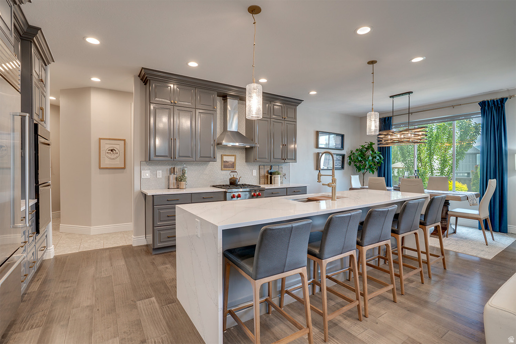 Open-concept kitchen featuring wood-finish flooring, an expansive island with a white countertop and integrated sink, stainless steel appliances, grey cabinetry, and recessed lighting