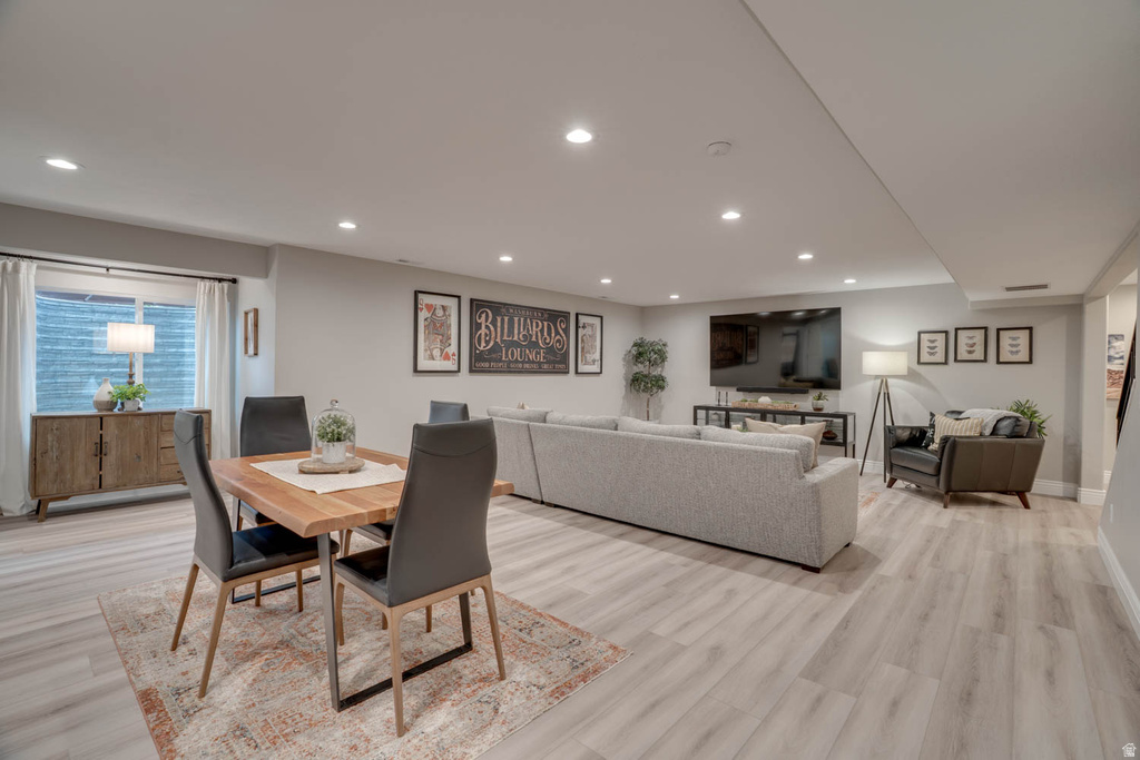 Spacious finished lower level featuring light wood-finish flooring, recessed lighting, a window with white drapery, and painted gray walls